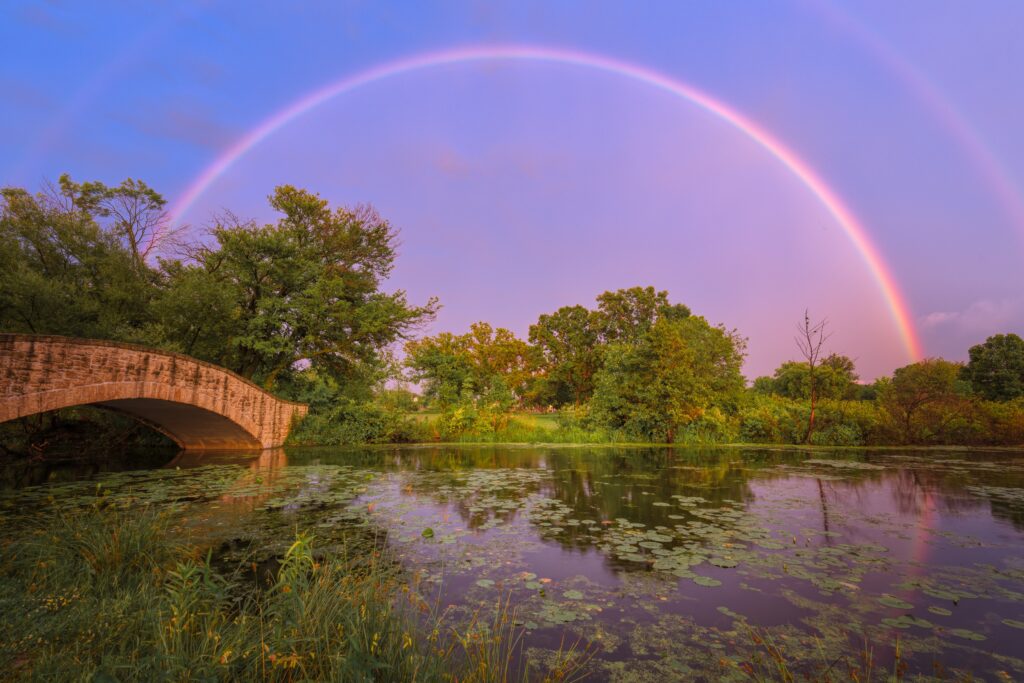 pont en pierre dans la nature avec un arc en ciel dans le ciel et des arbres verts